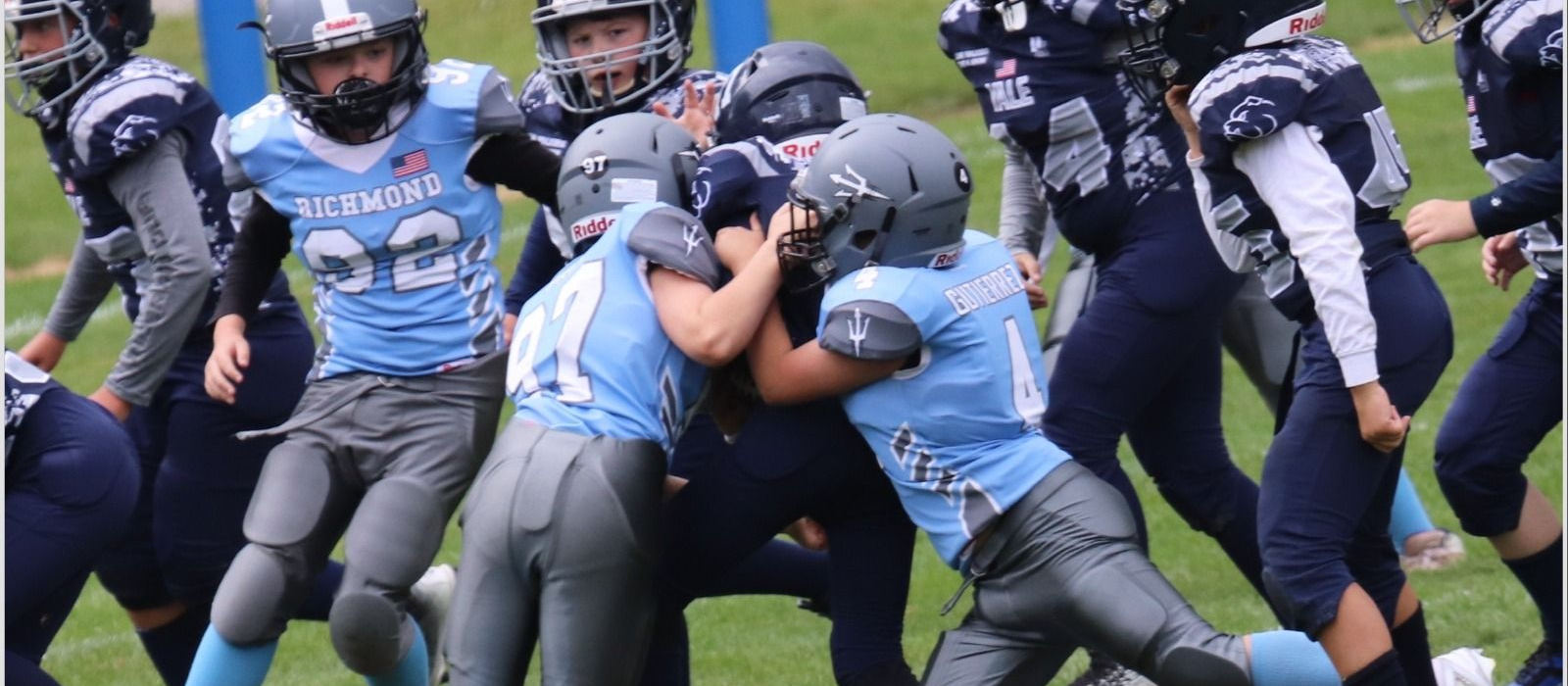 Football player in silver uniform runs with ball on a green field.