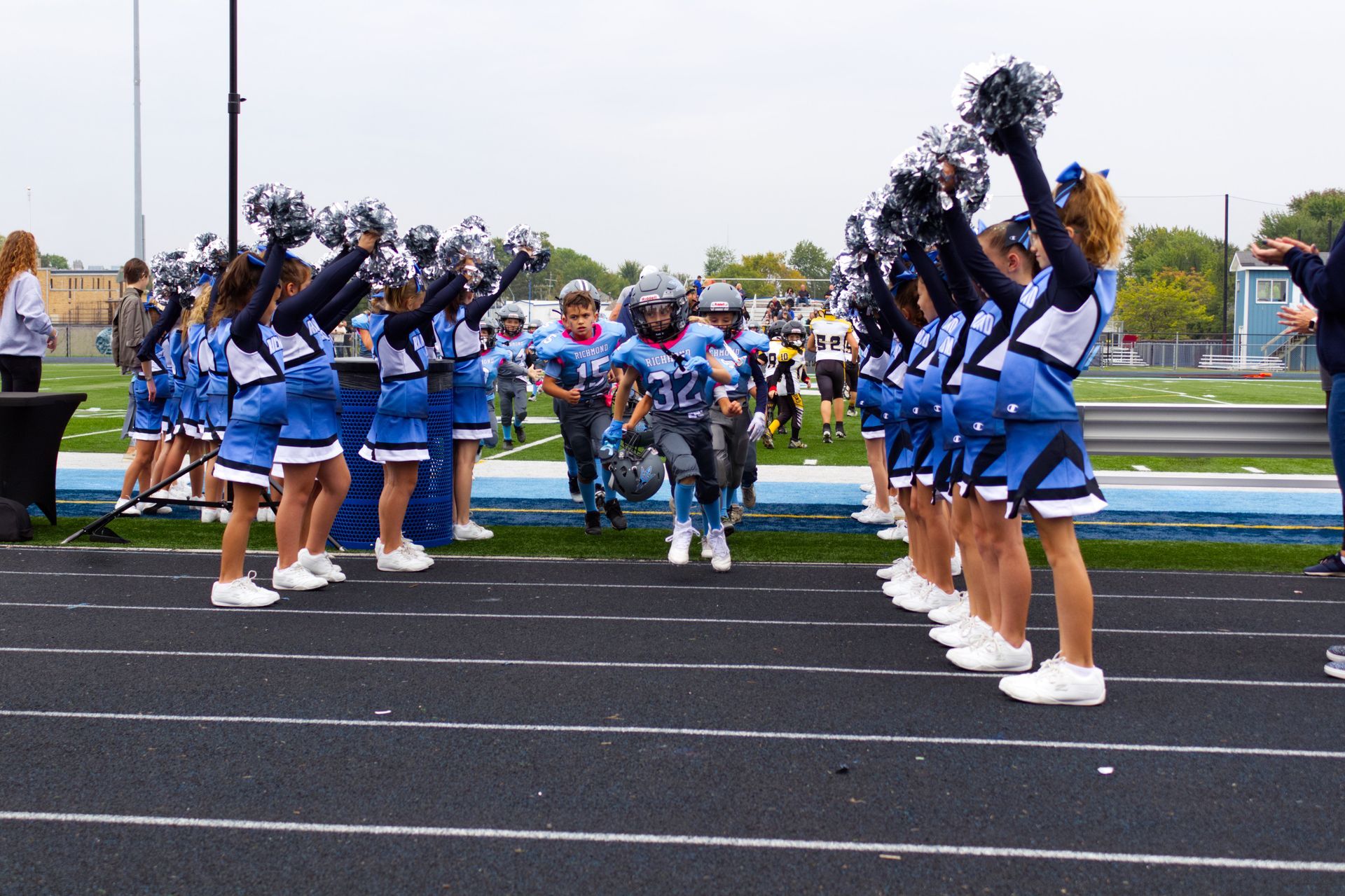 Football player in maroon jersey holding ball, smiling, surrounded by teammates on a field.