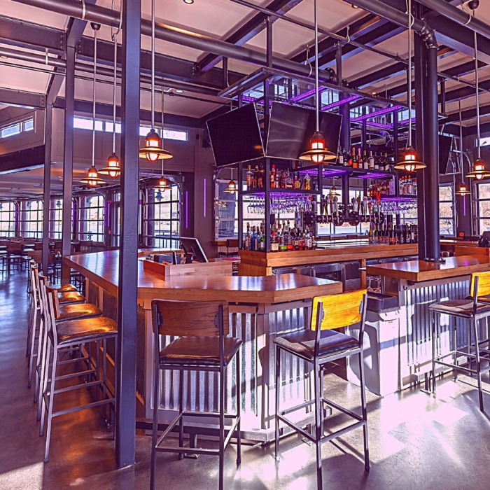 Interior of a modern bar with a long counter, bar stools, and industrial design elements.