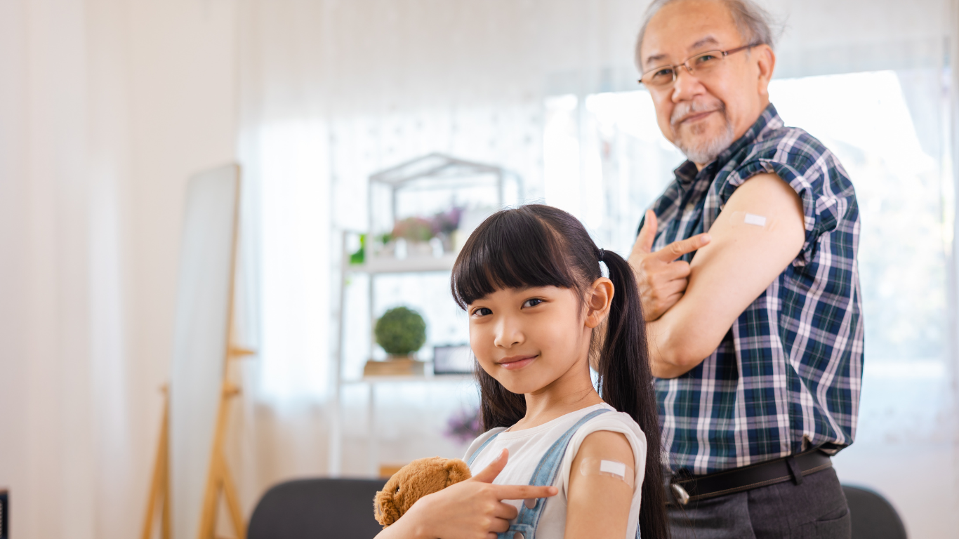 A little girl is pointing at her grandfather 's arm after getting a vaccine.