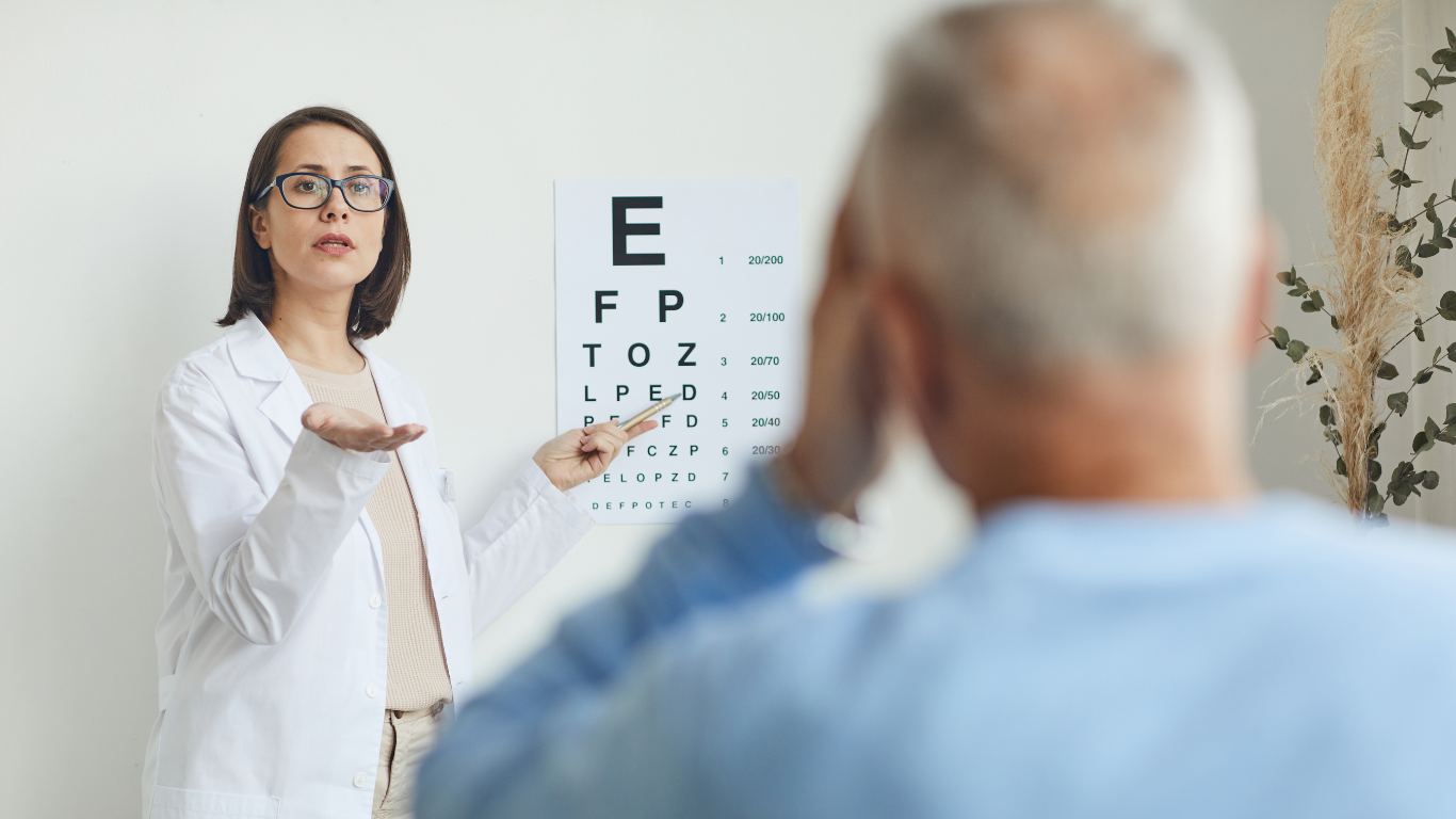 Optometrist pointing to eye chart during an exam with a patient in white room.
