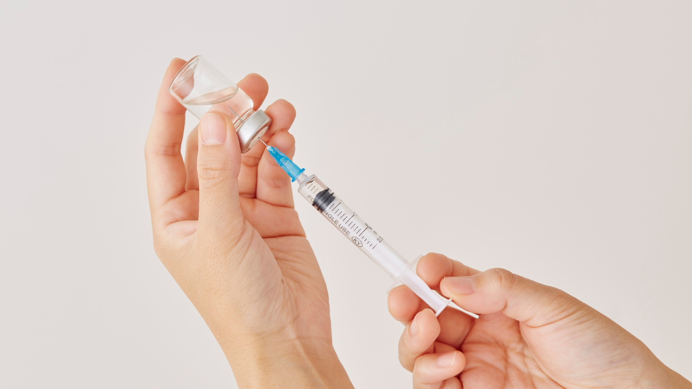 A person is holding a syringe and a bottle in their hands.