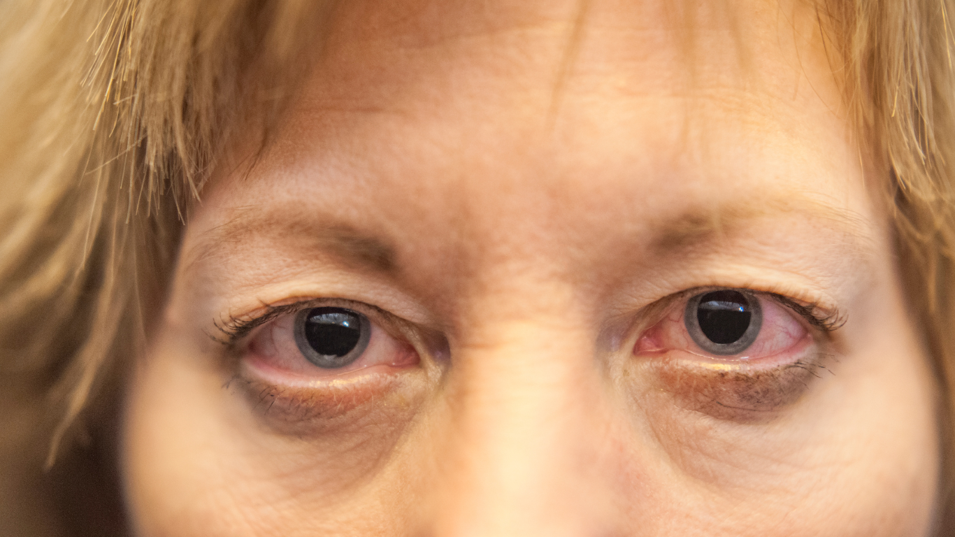 An elderly woman is wearing glasses and smiling.