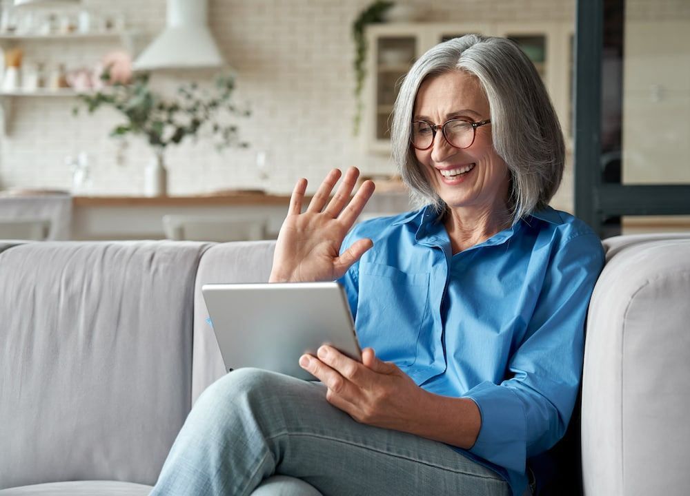 An older woman is sitting on a couch using a tablet computer.