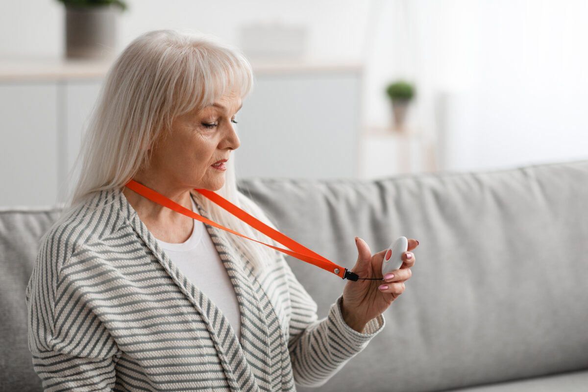 An elderly woman is sitting on a couch with a lanyard around her neck.