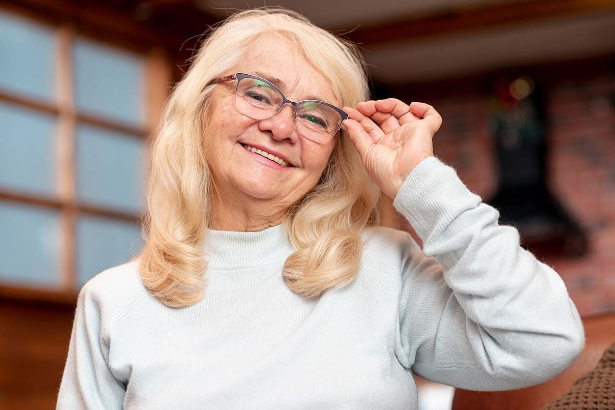 An elderly woman is wearing glasses and smiling.
