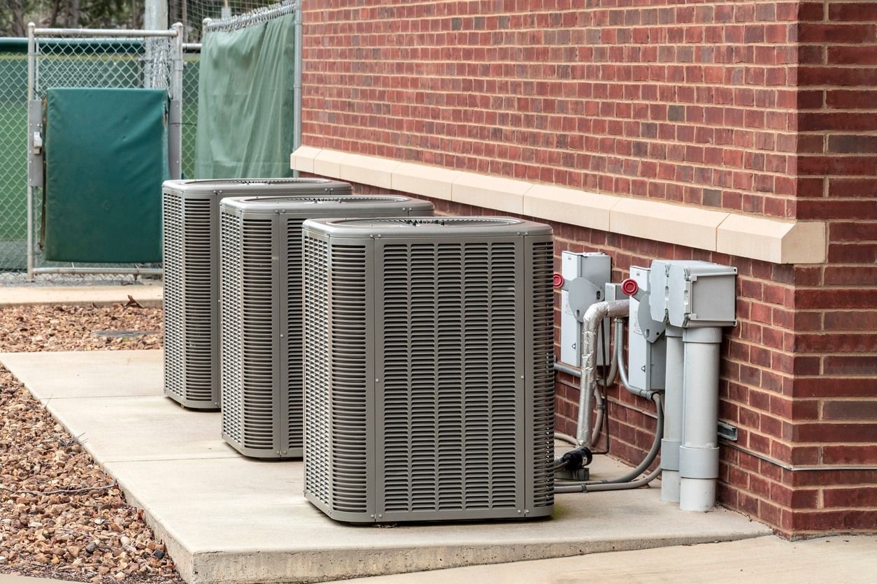 Three air conditioners are lined up on the side of a brick building.
