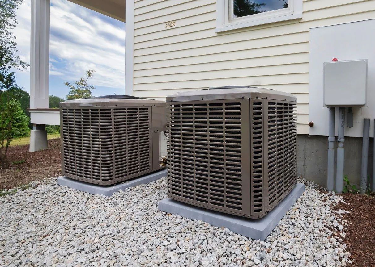 Two outdoor air conditioning units next to a house, sitting on concrete pads, with gravel
ground c