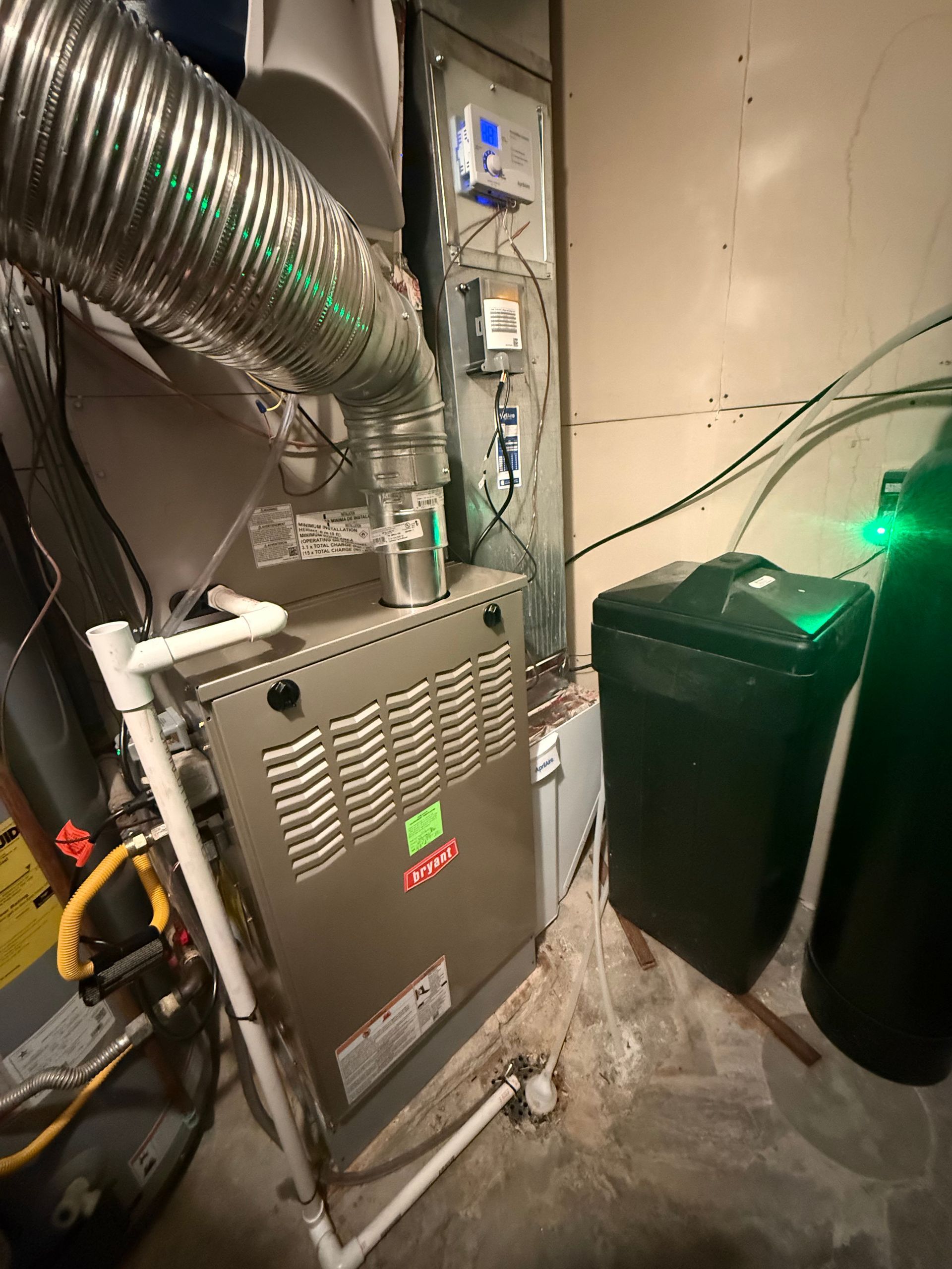 A furnace is sitting in a basement next to a water heater.