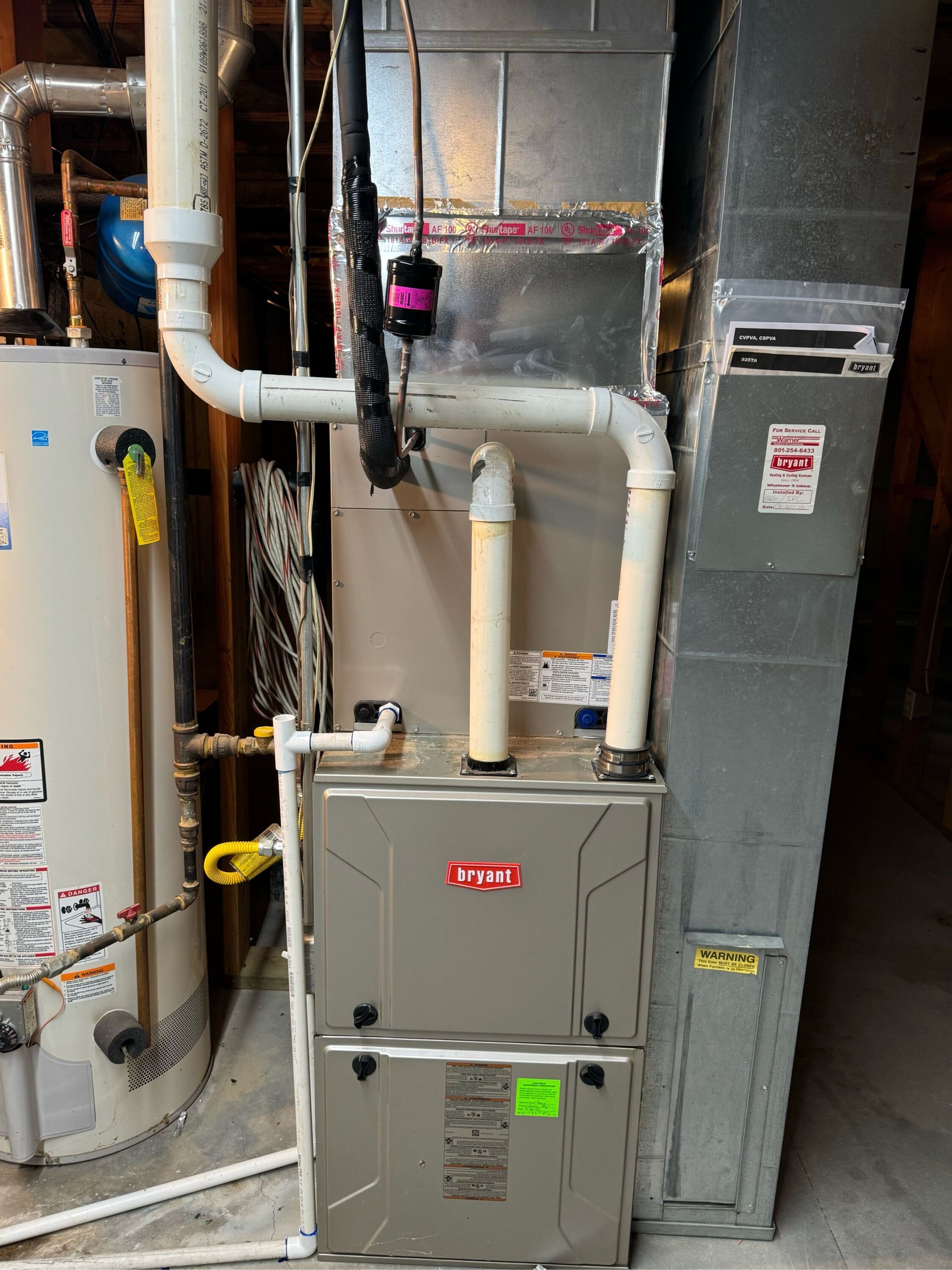 A furnace is sitting in a basement next to a water heater.