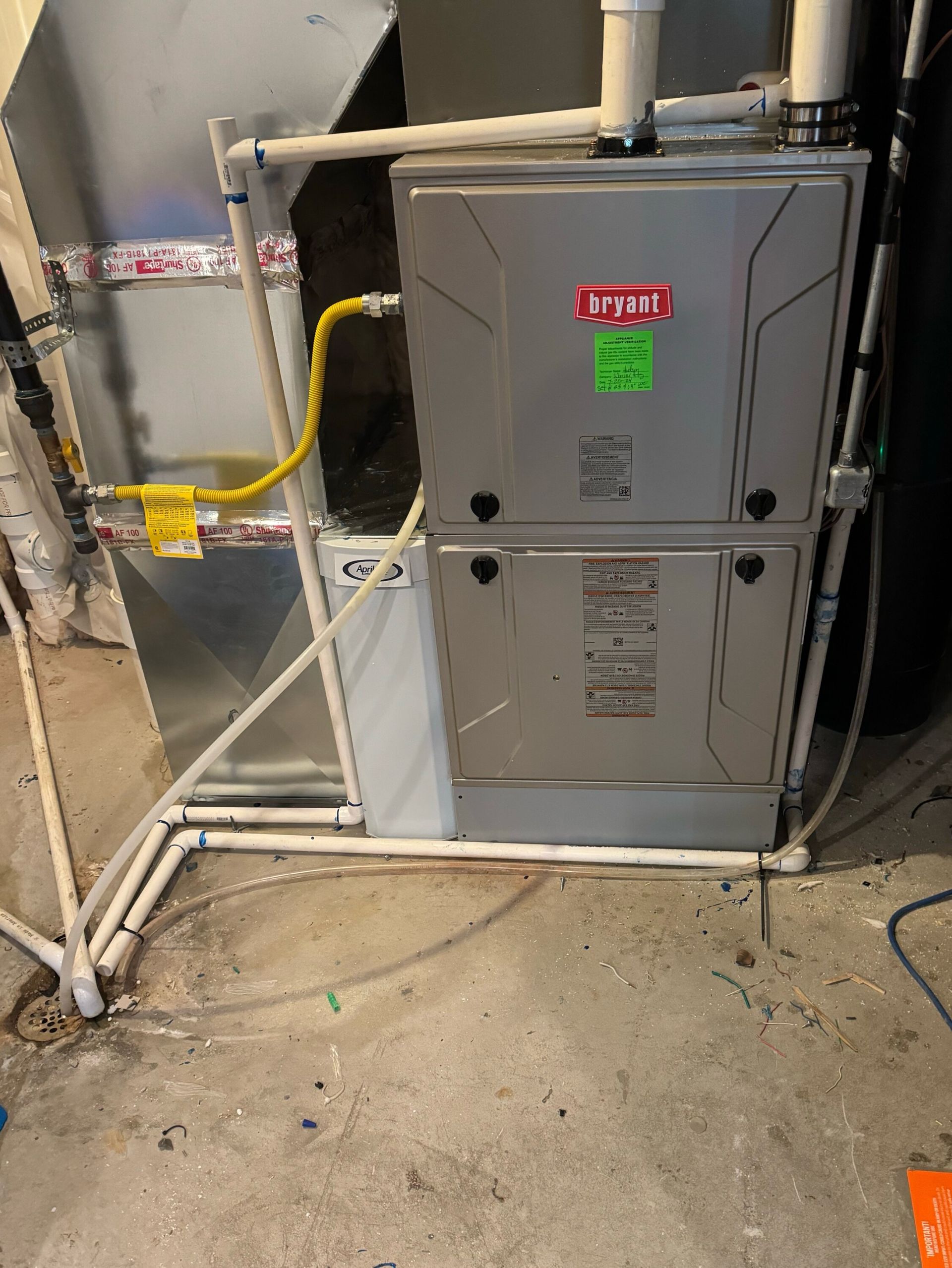 A furnace is sitting in a basement next to a pipe.