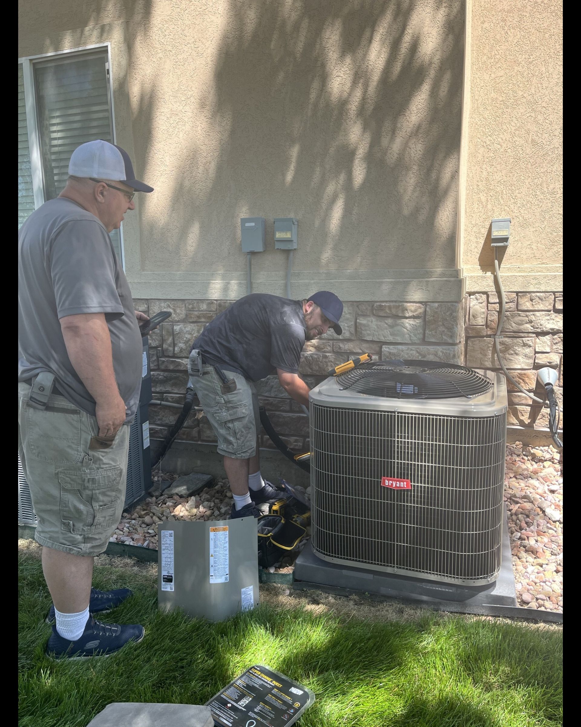 Two men are working on an air conditioner outside of a house.