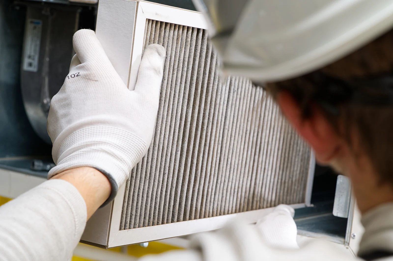 Person in a hard hat and gloves replacing a dirty air filter in an HVAC unit.