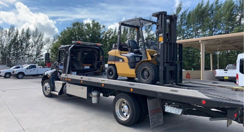 Black Truck Towing a Forklift  | Naples Towing & Recovery
