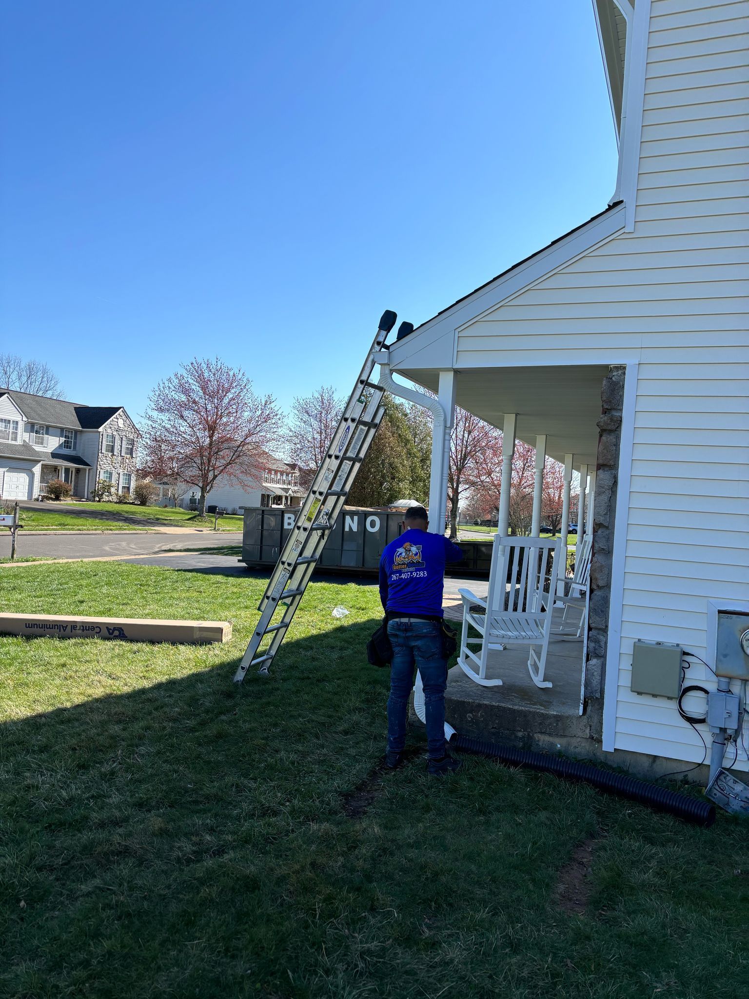 Person on a ladder near a house, preparing to work on the roof of the porch, on a sunny day.