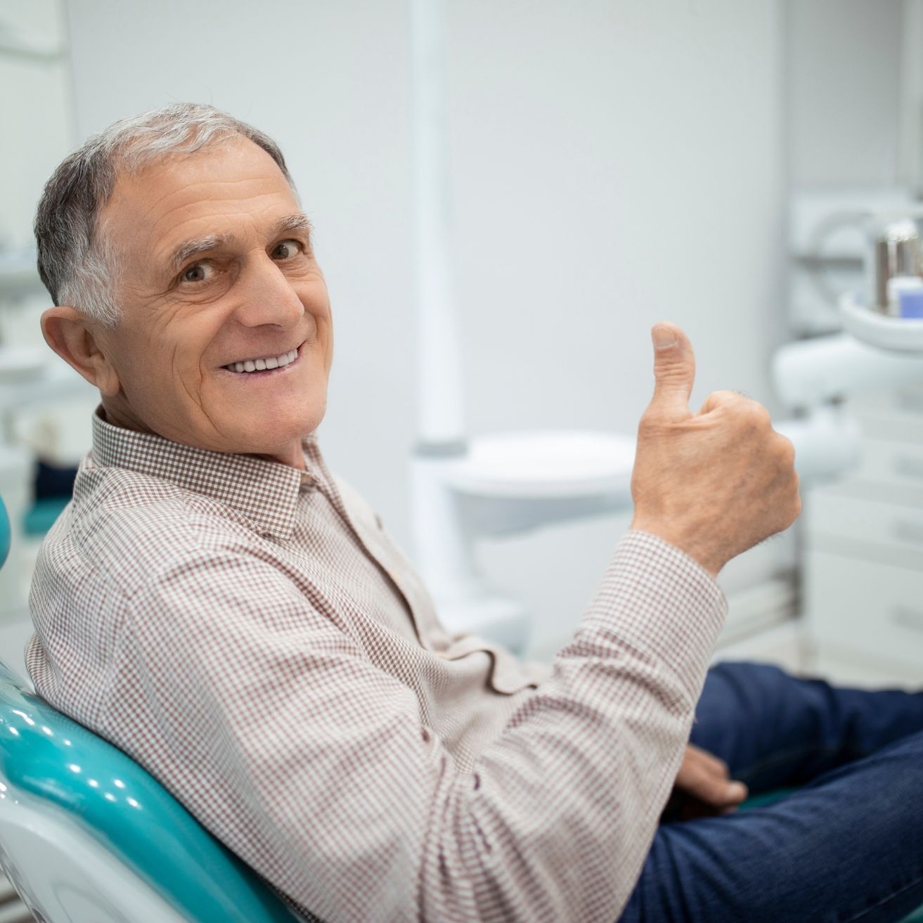 Man in dental chair giving a thumbs up, smiling. Clinic setting.