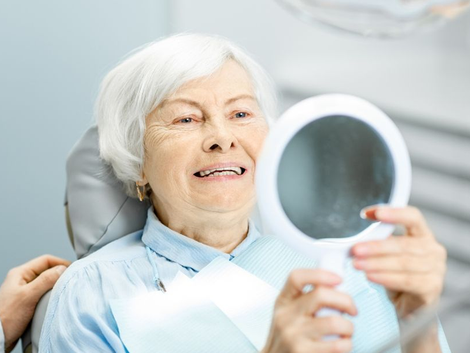 Senior woman in dentist chair looking at her teeth in a hand mirror.