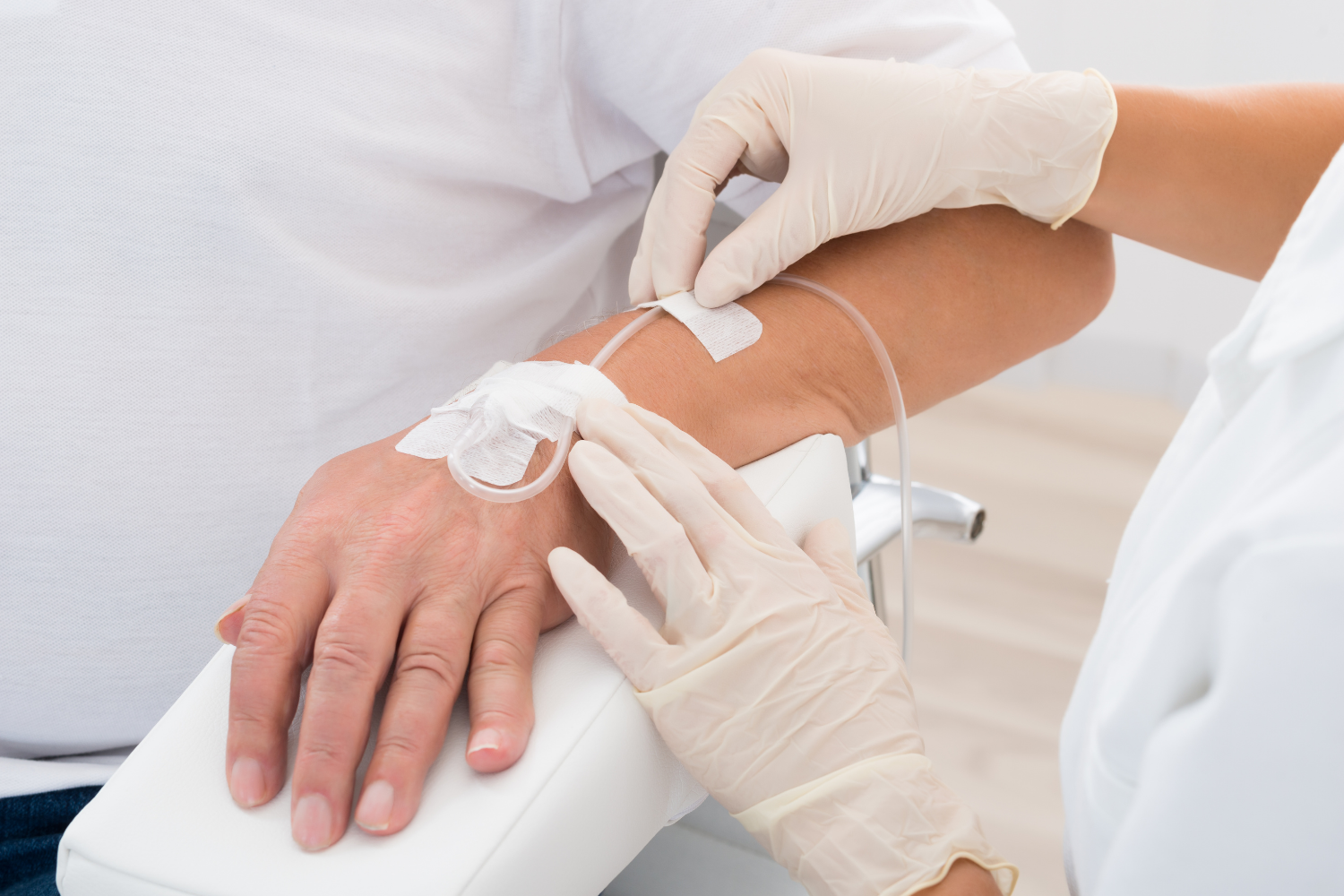 A person receiving intravenous fluids; a gloved hand adjusts the IV line on the patient's arm.