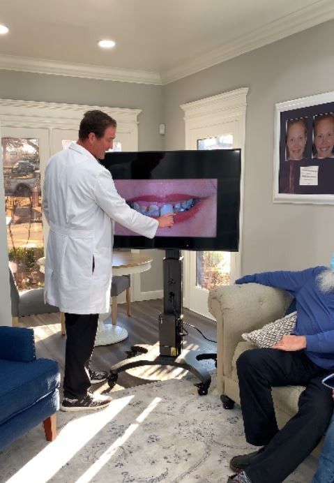 Dentist pointing at teeth on a screen during a consultation in an office.