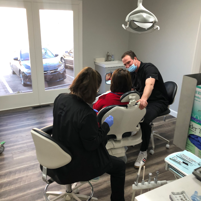 Dental exam: Dentist and assistant with a patient in a chair. Office setting, window behind them.