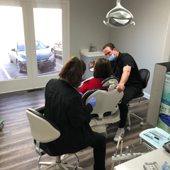Dental exam: Dentist and assistant with a patient in a chair. Office setting, window behind them.