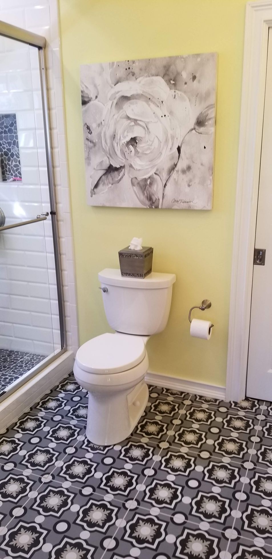 A bathroom with a toilet , shower , and a painting on the wall.