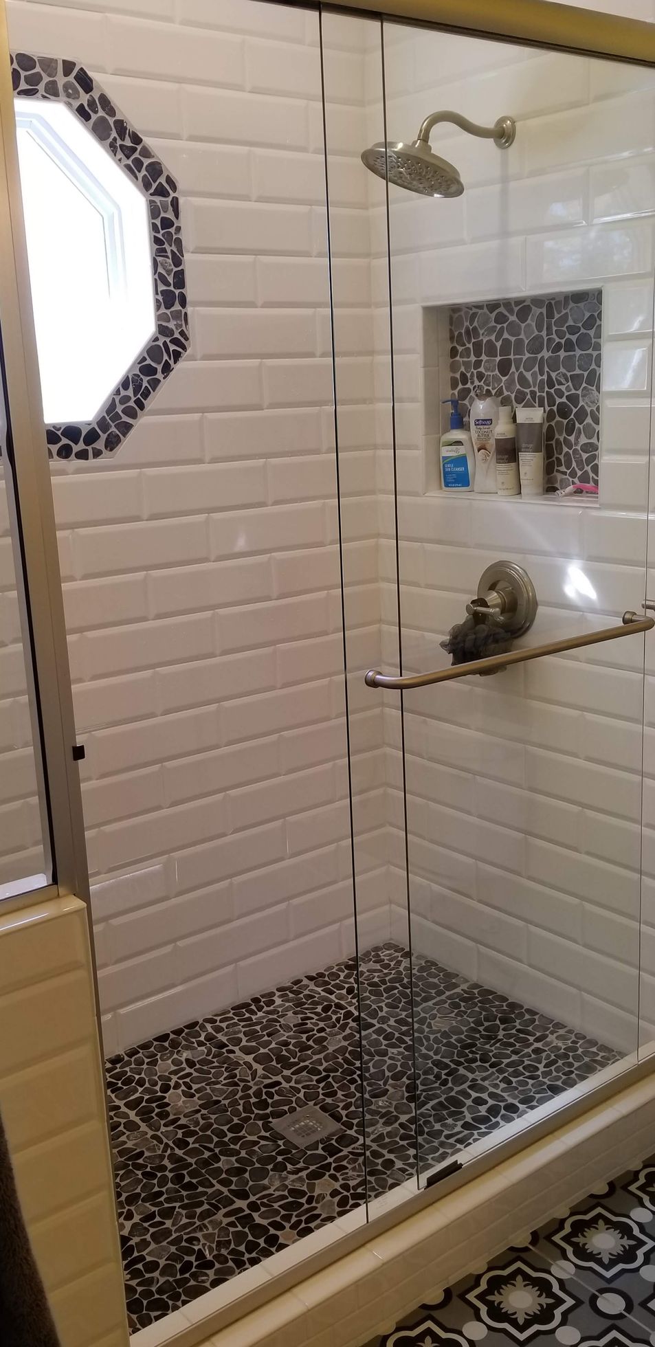 A bathroom with white tiles and a walk in shower with a glass door.