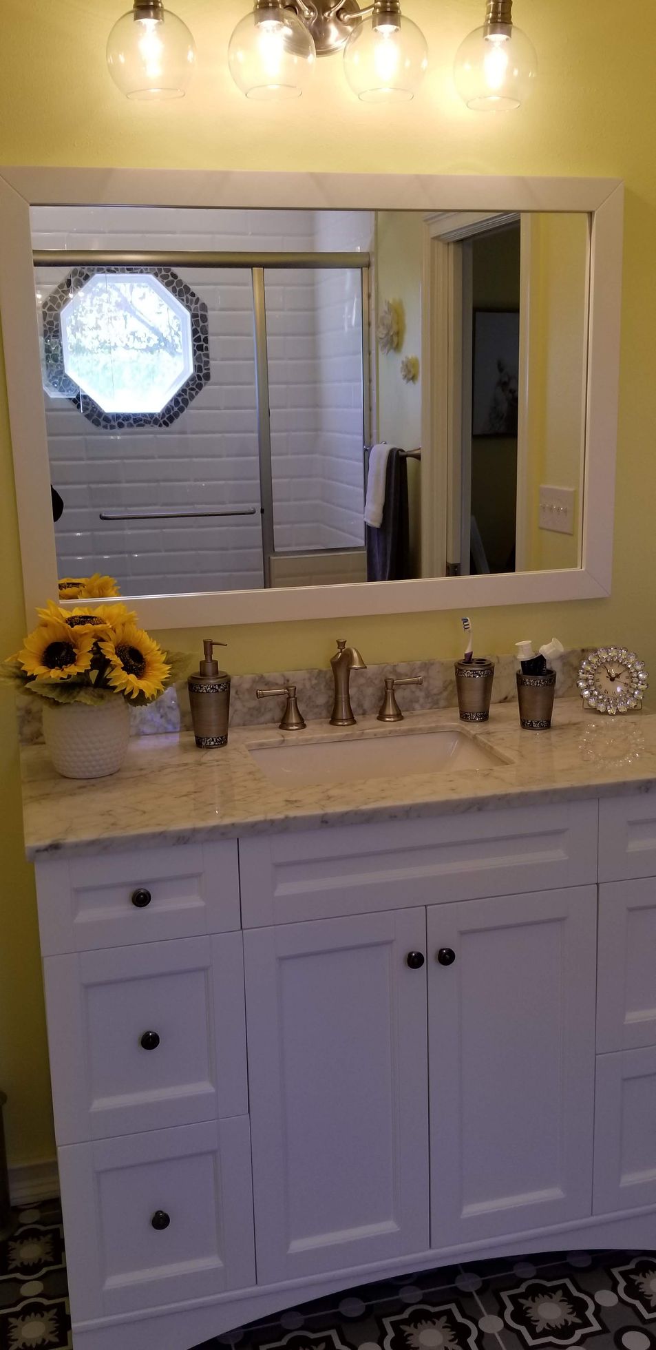 A bathroom with a vanity , sink , mirror and sunflowers.