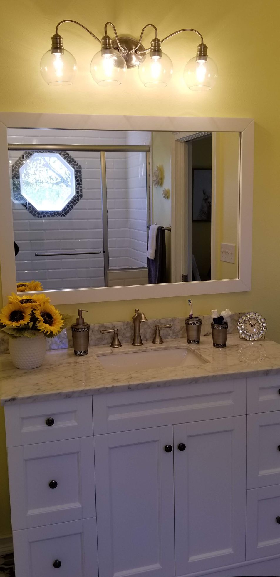 A bathroom with two sinks , a mirror , and a vase of sunflowers.