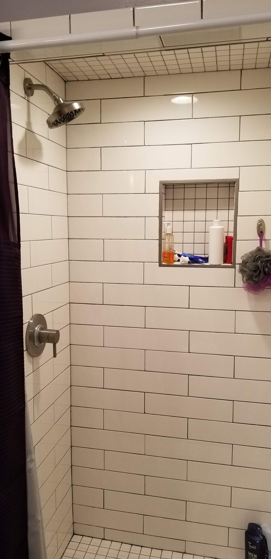 A shower with white tiles and a purple shower curtain.