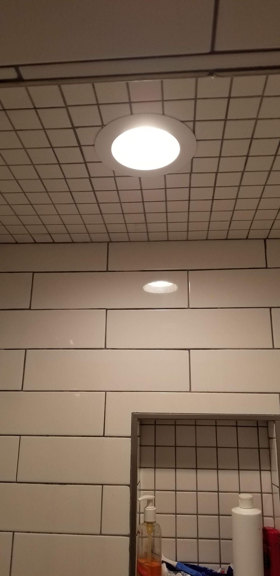 A bathroom with white tiles and a light on the ceiling.