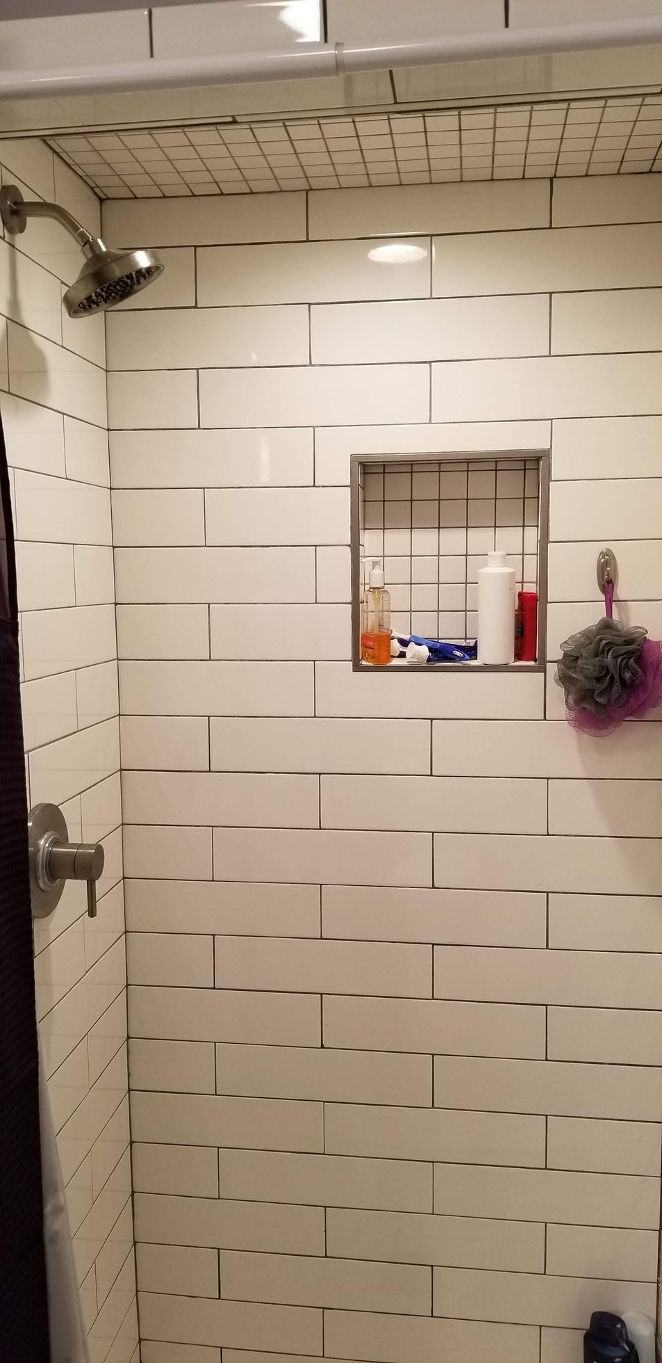 A bathroom with white tiles and a shower head.