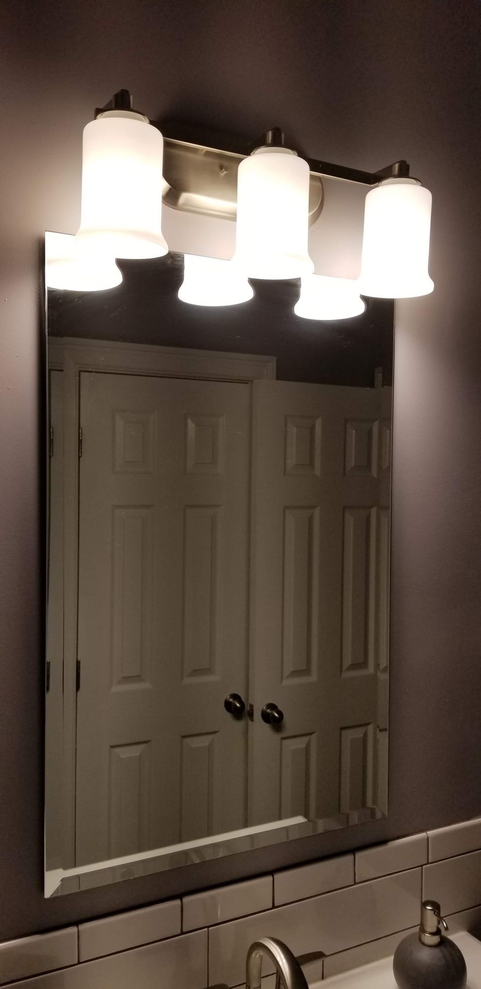 A bathroom mirror with lights above it and a door in the background.
