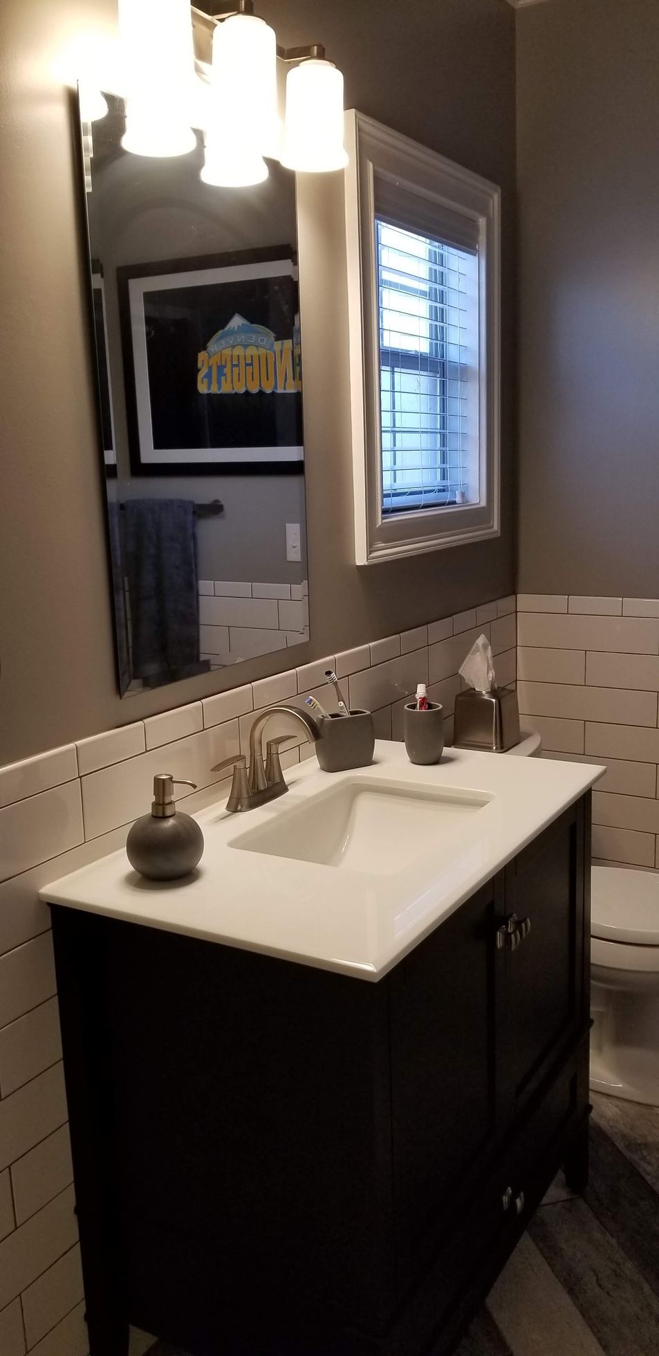 A bathroom with a sink , toilet , mirror and window.