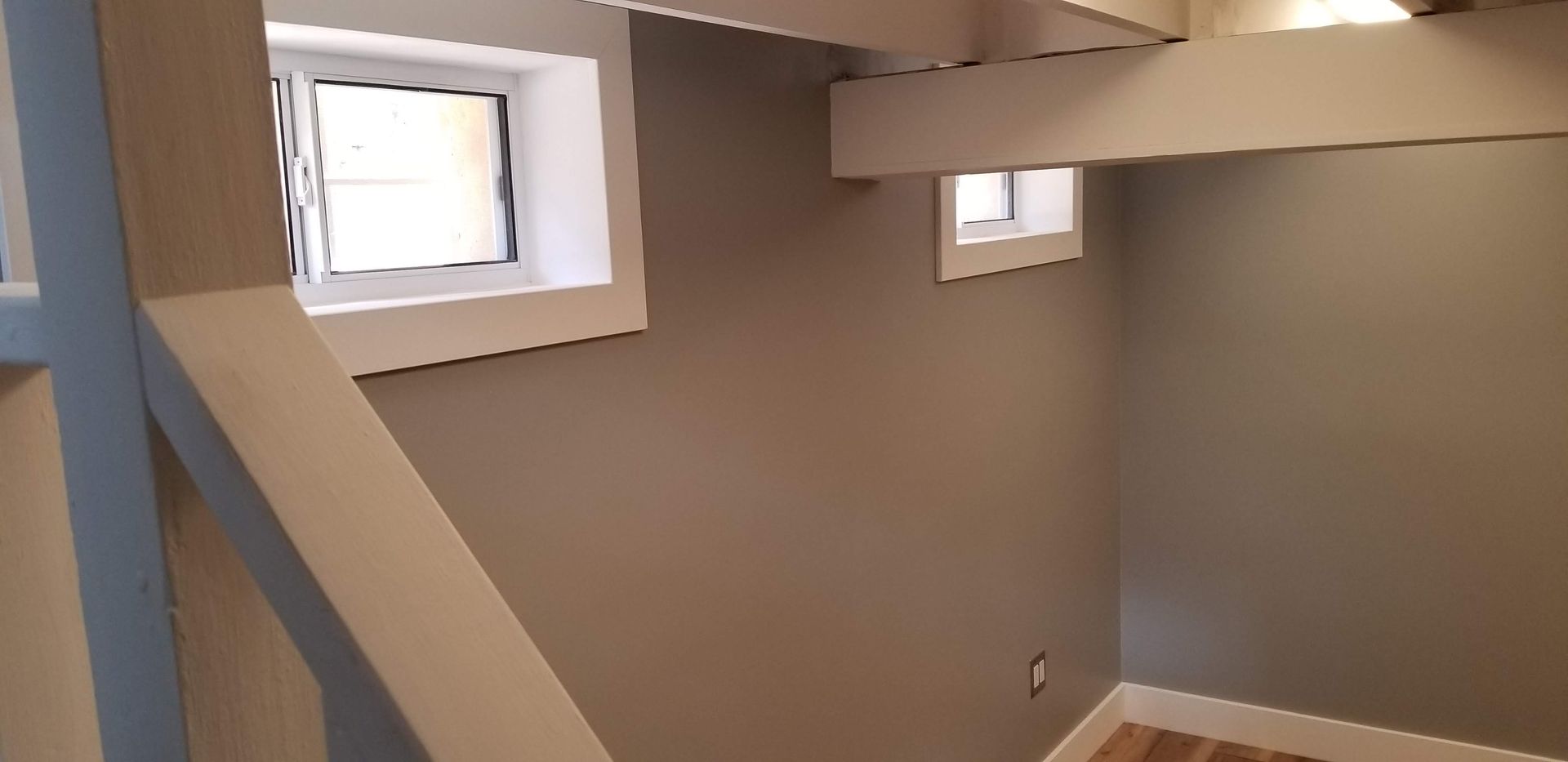 A room with a staircase and two windows on the wall.