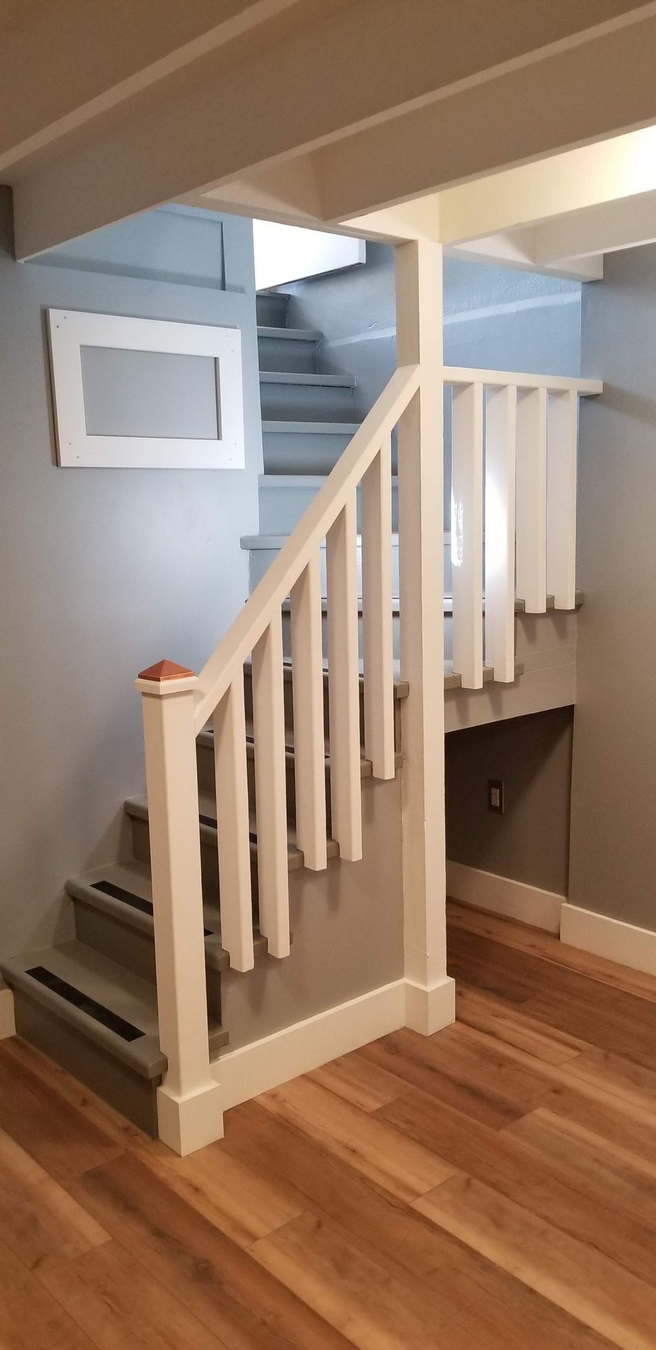 A staircase in a basement with wooden floors and a white railing.
