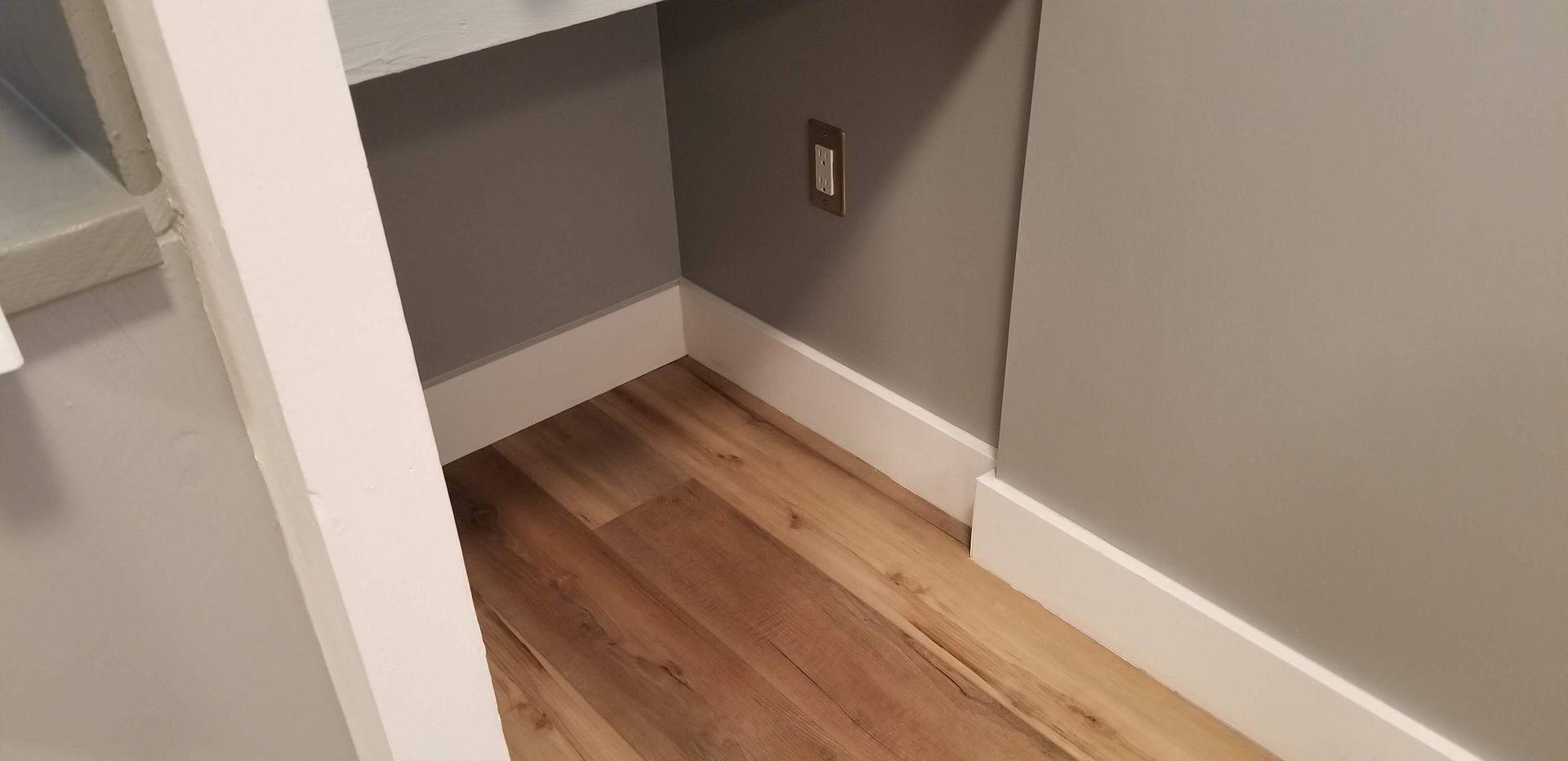 A corner of a room with hardwood floors and gray walls.