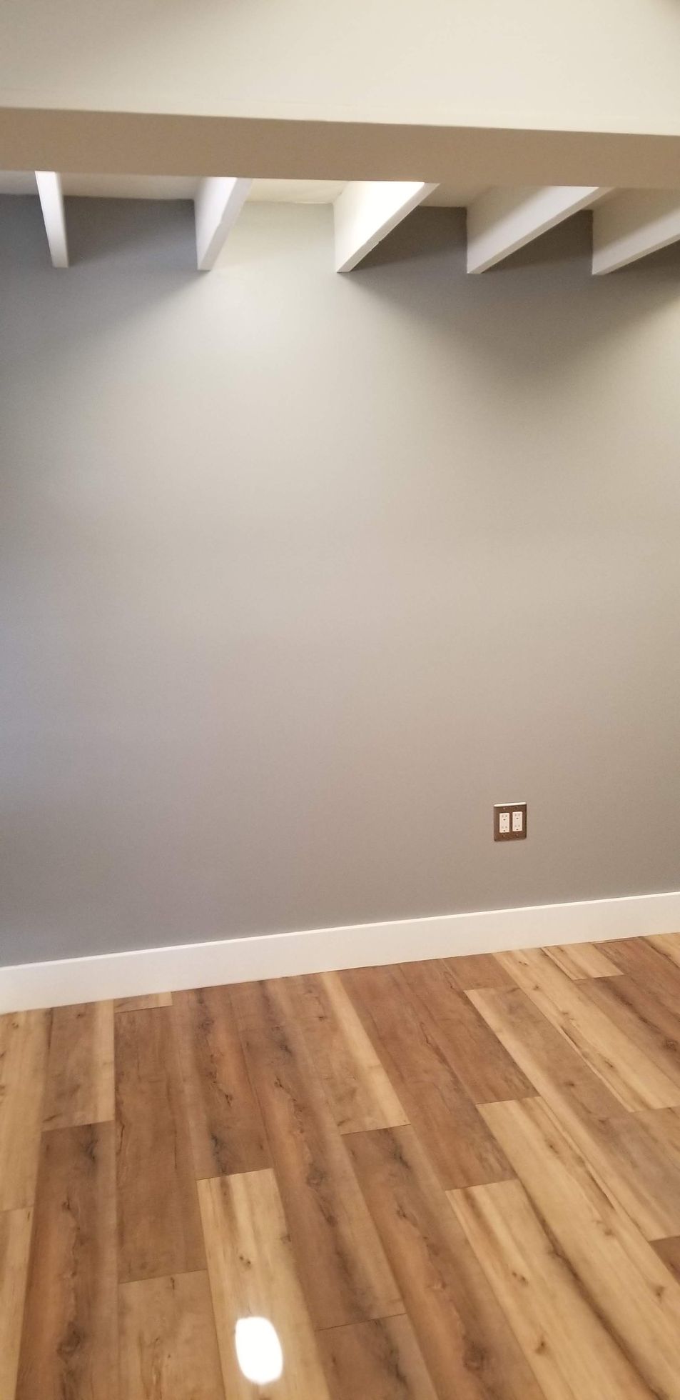 An empty room with a wooden floor and a gray wall.