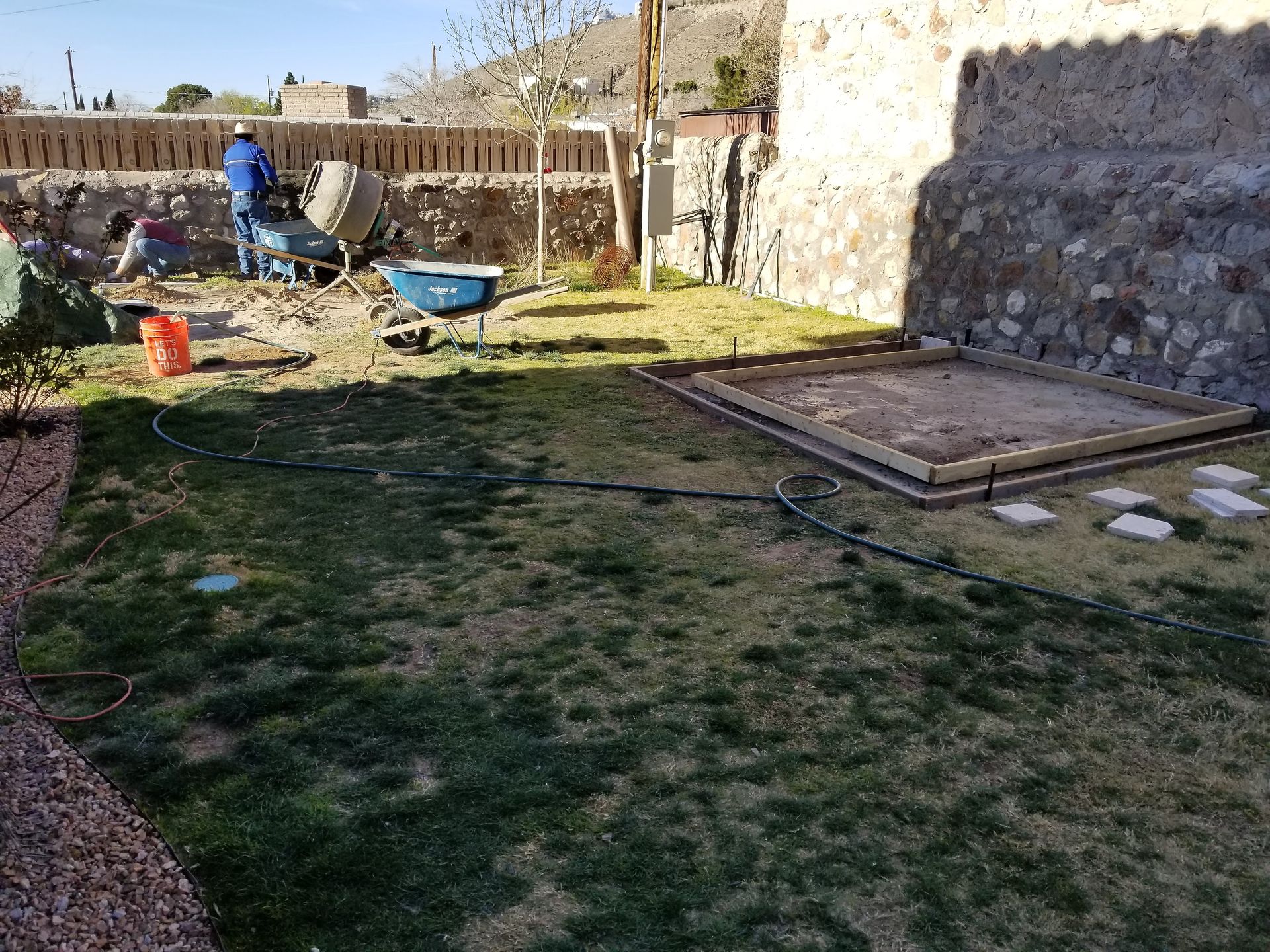 A man is pushing a wheelbarrow in a backyard.