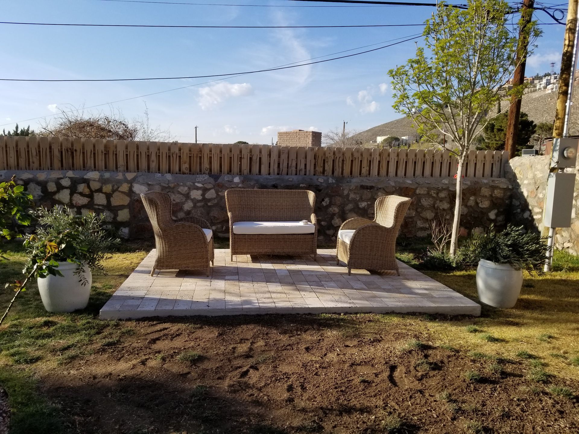 A patio with wicker furniture and potted plants in front of a stone wall.