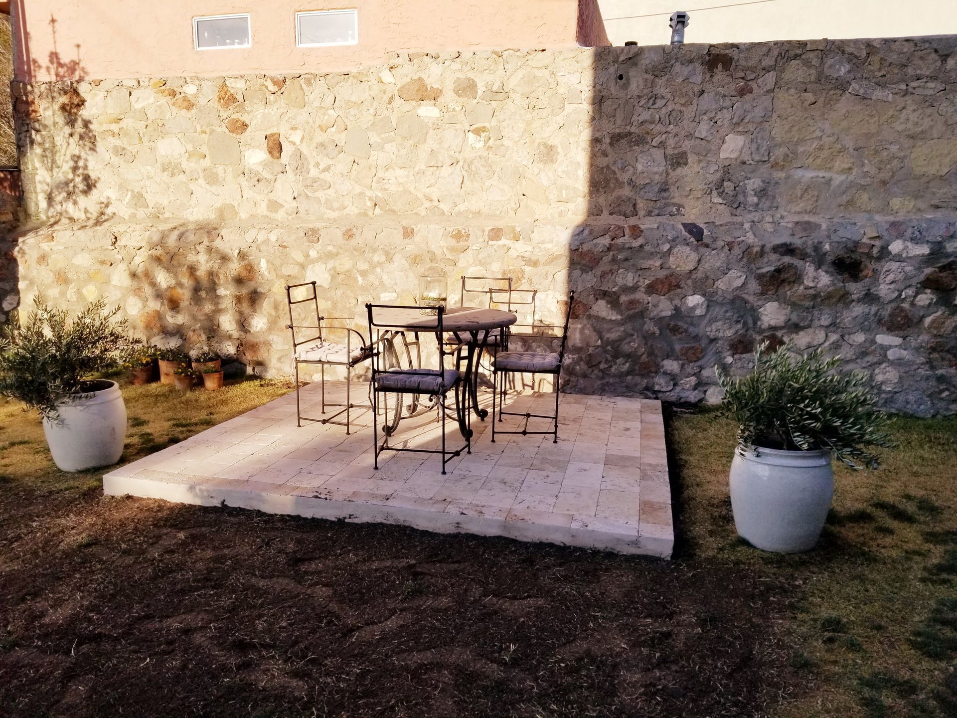 A patio with a table and chairs in front of a stone wall