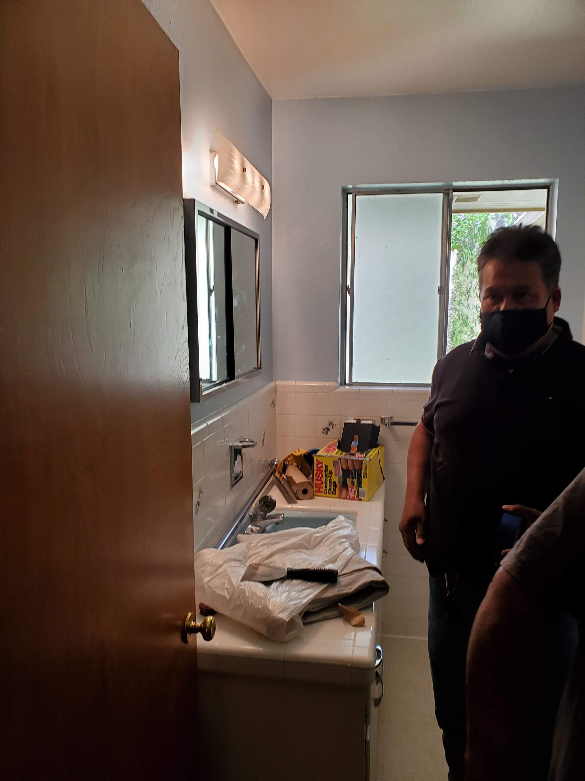 A man wearing a mask is standing in a bathroom.