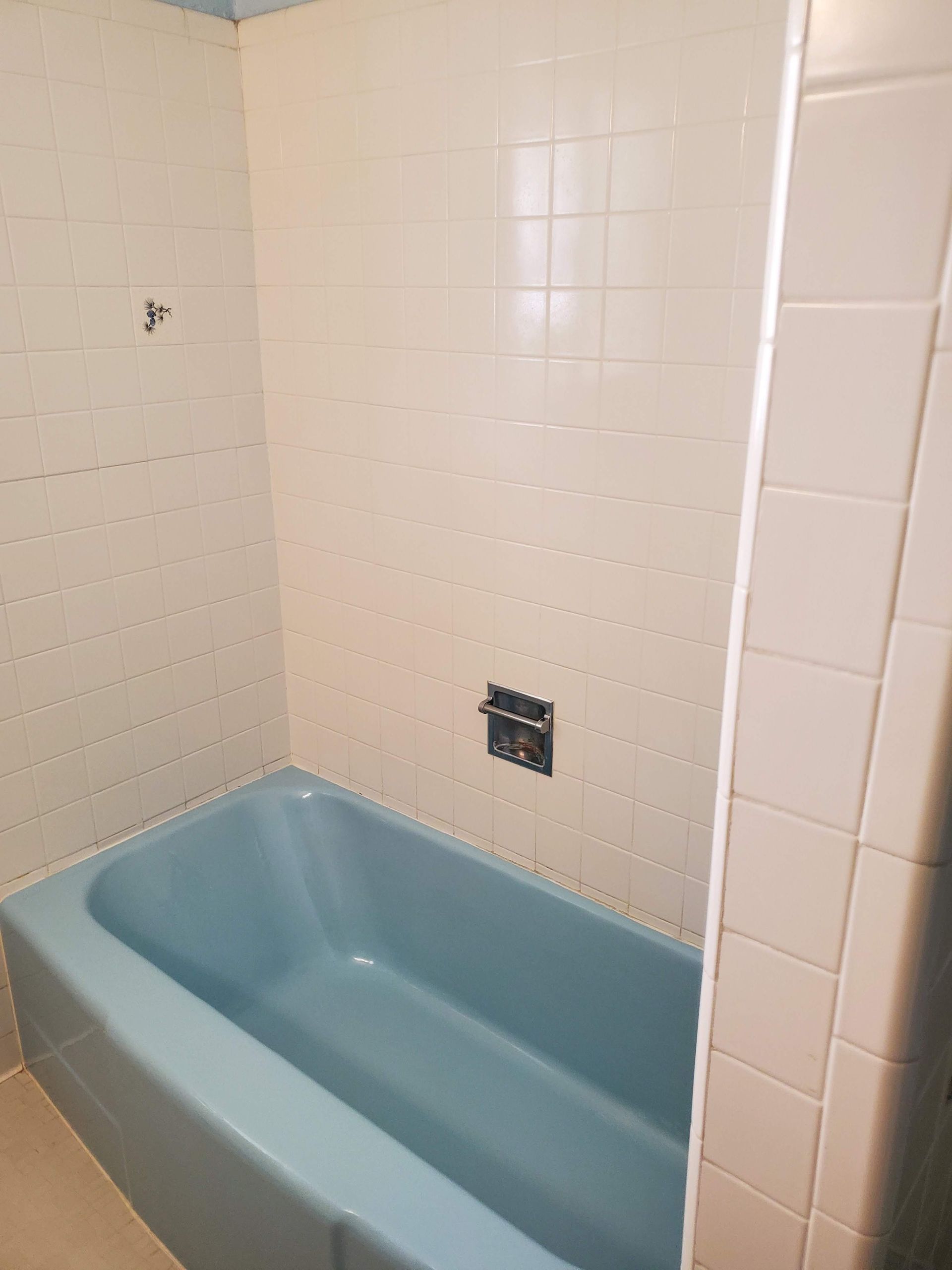 A blue bathtub in a bathroom with white tiles.