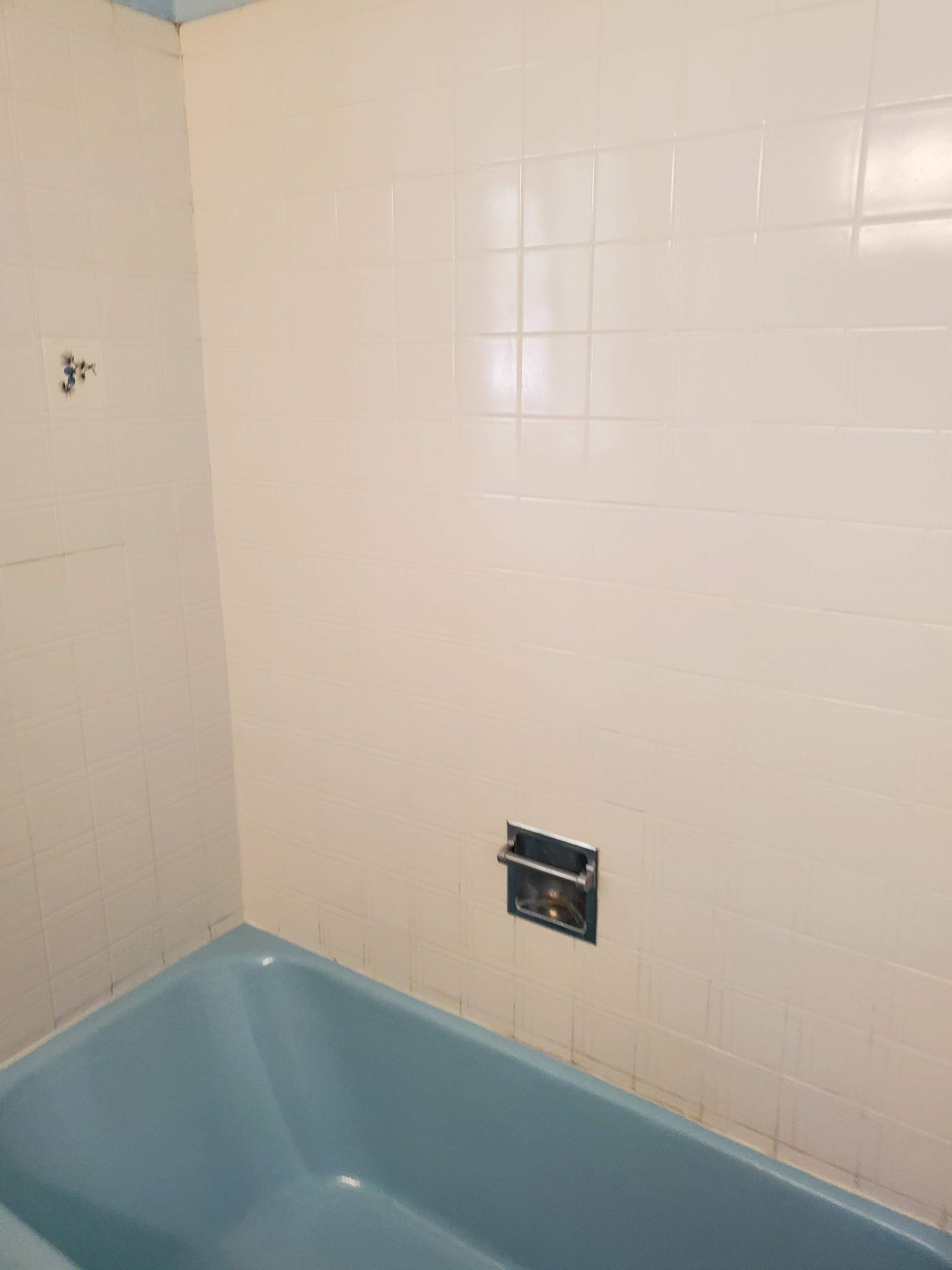 A blue bathtub in a bathroom next to a white tiled wall.