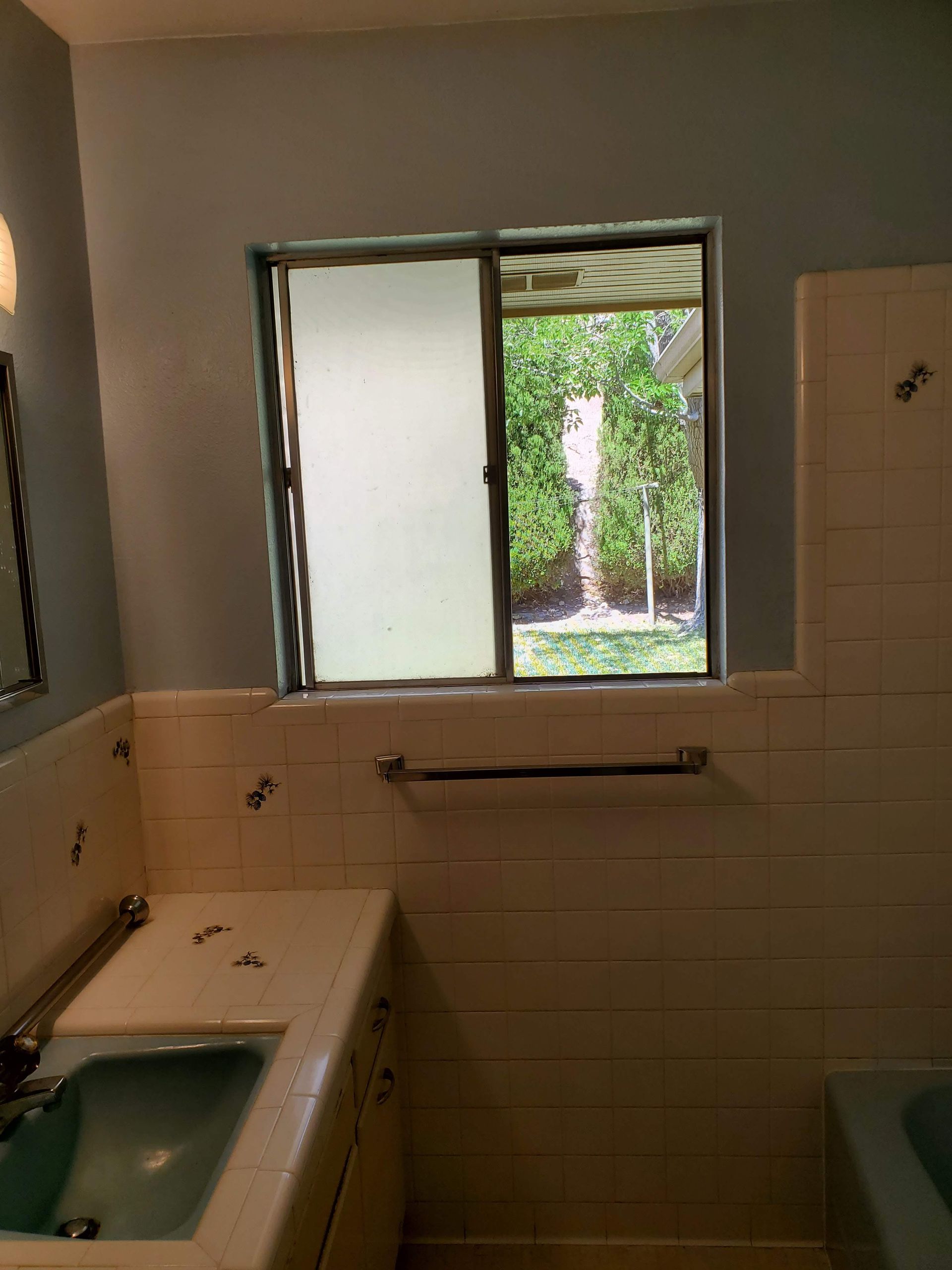 A bathroom with a sink and a window with a view of a garden.
