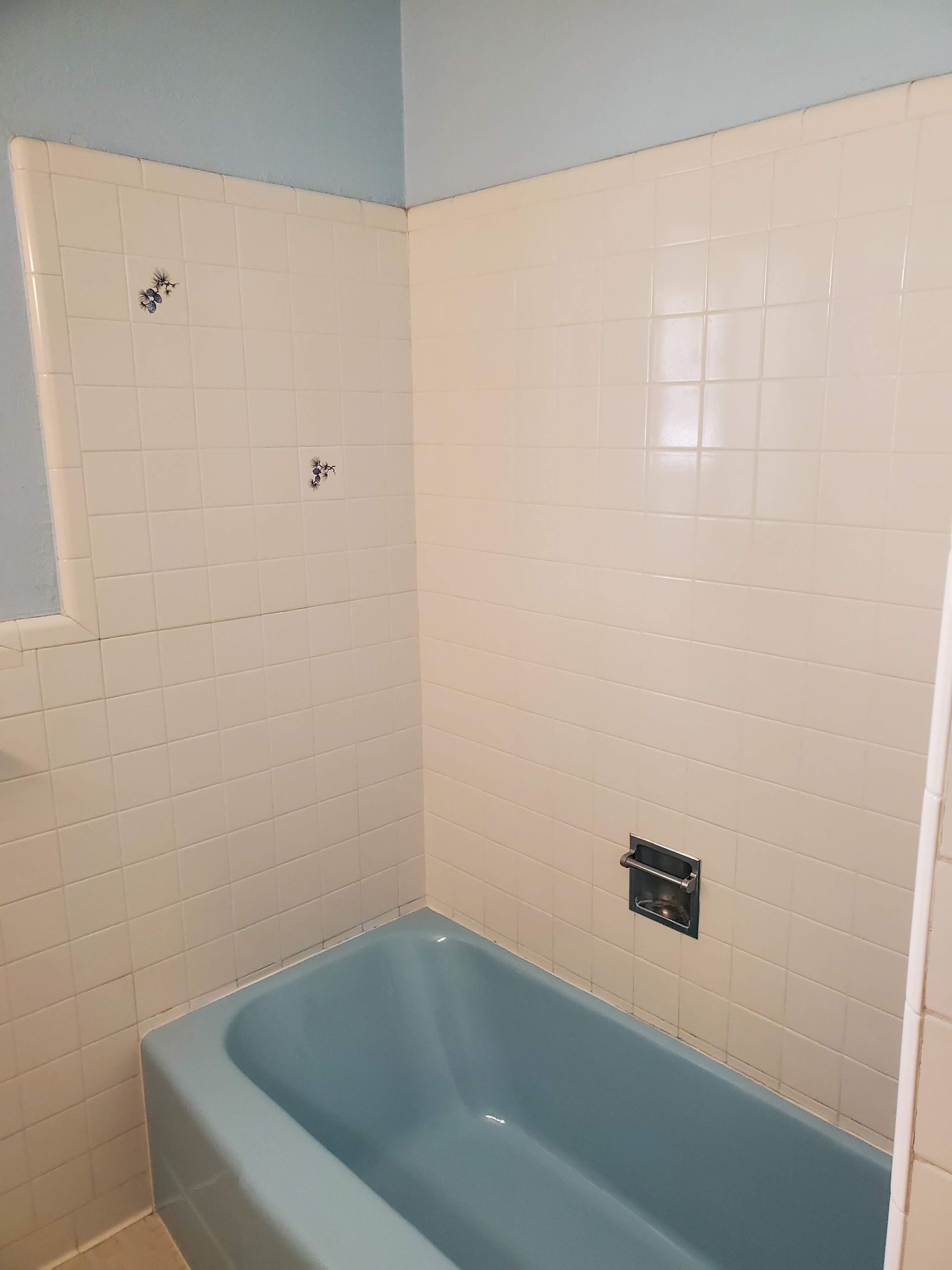 A bathroom with a blue bathtub and white tiles.