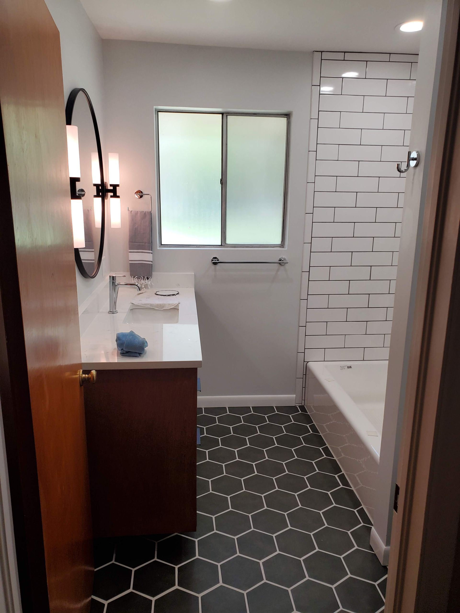 A bathroom with a sink , tub , mirror and window.