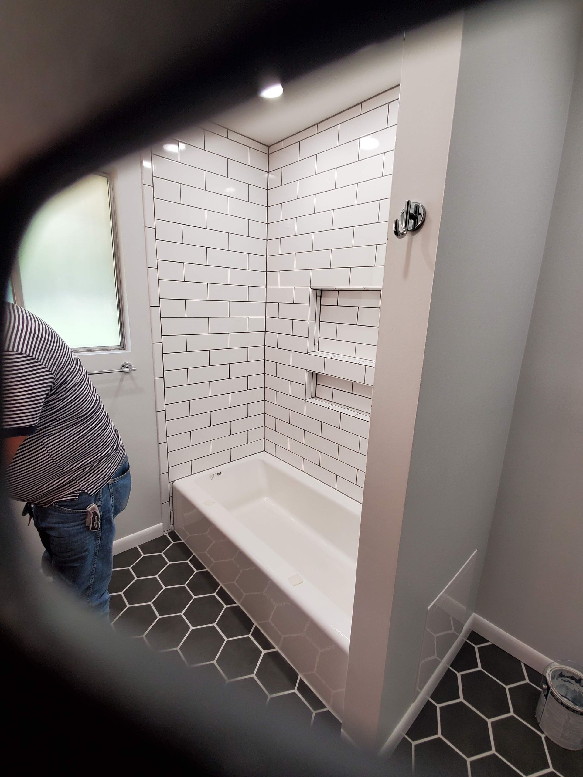 A person is standing in a bathroom with a bathtub and shower.