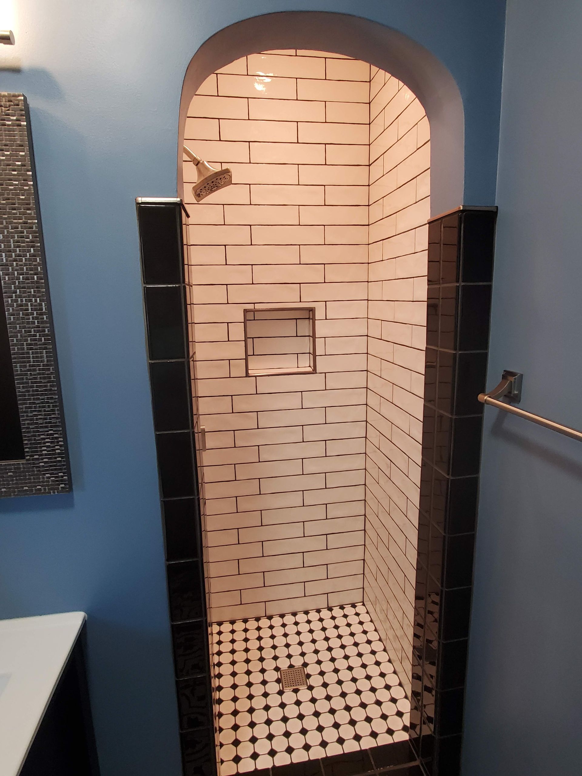 A bathroom with a walk in shower with black and white tiles