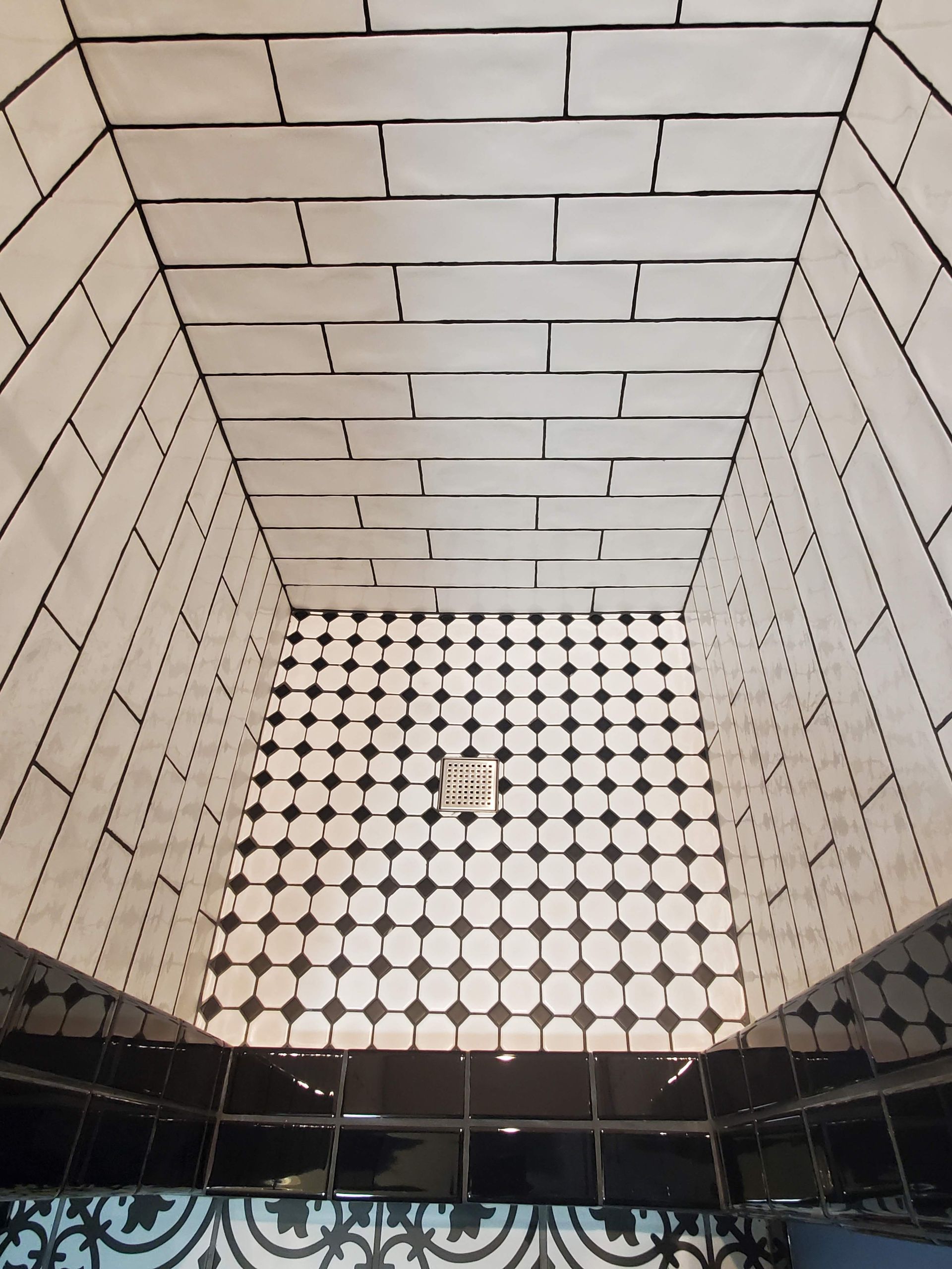 A bathroom with black and white tiles and a drain